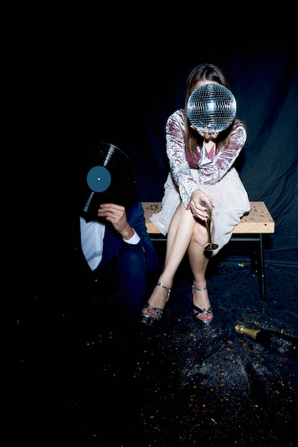 Couple couvrant les visages avec boule disco et disque vinyle à la fête