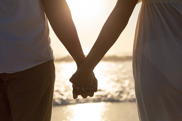 Couple debout ensemble main dans la main sur la plage