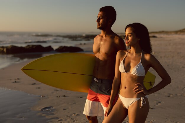 Couple debout avec planche de surf sur la plage