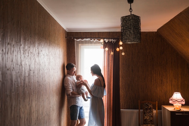 Photo gratuite couple debout près de la fenêtre jouant avec leur bébé à la maison