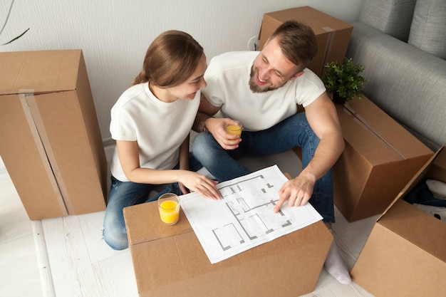 Couple discuter de plan de maison assis sur le sol avec des boîtes de déménagement