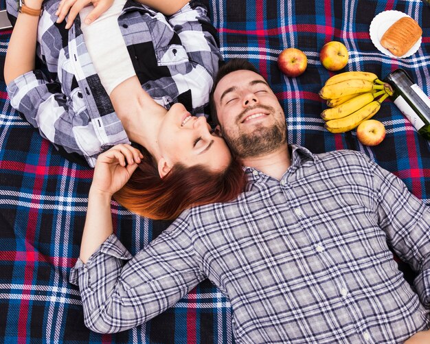 Couple dormant sur une couverture avec beaucoup de fruits; pâte feuilletée et bouteille de champagne