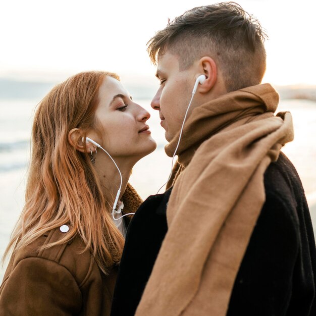 Couple écoutant de la musique sur des écouteurs ensemble sur la plage en hiver