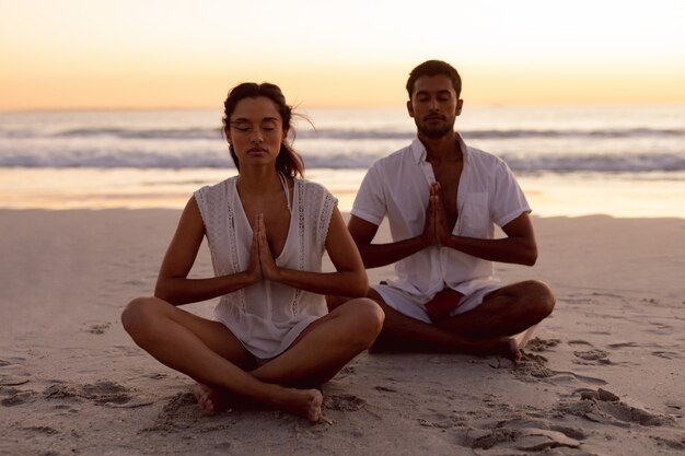 Couple effectuant le yoga ensemble sur la plage