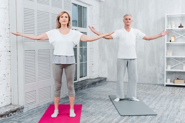 Couple effectuant le yoga en tendant les bras debout sur un tapis de yoga