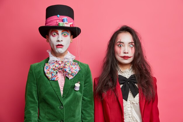 Un couple effrayant choqué célèbre Halloween se maquille professionnel et porte des costumes posés côte à côte contre un mur rose