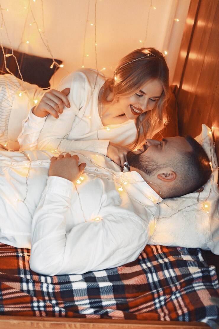 Photo gratuit couple élégant assis avec une guirlande à la maison sur un lit