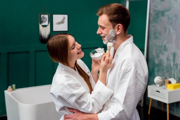 Photo gratuite couple embrassé dans des peignoirs appliquant de la mousse à raser