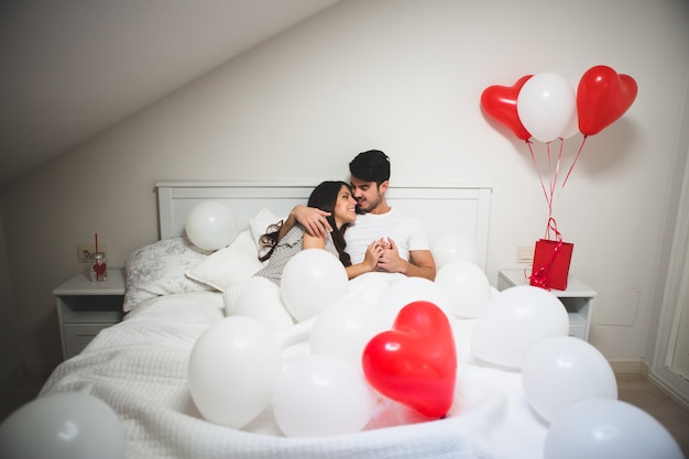 Couple enlacé dans son lit entouré de ballons