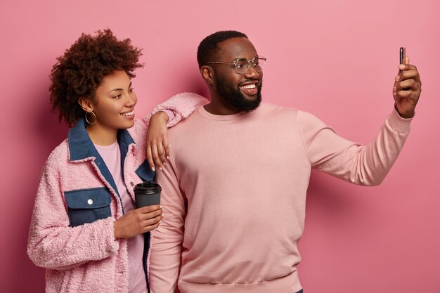 Un couple ethnique positif se tient près l'un de l'autre, fait un selfie