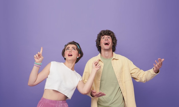 Couple étonné pointant les mains vers le haut pour un espace vide isolé sur fond violet