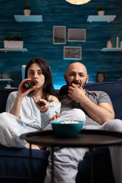 Couple excité détendu regardant la télévision sur un canapé relaxant tard dans la nuit