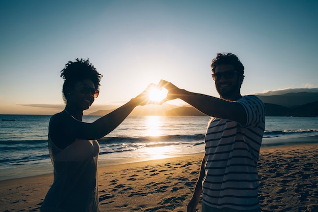 Couple faisant du coeur avec les mains au coucher du soleil