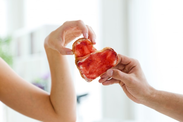 Couple faisant signe de coeur avec deux tranches de pain avec de la confiture.