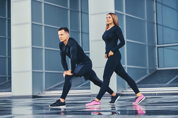 Photo gratuite le couple de fitness athlétique s'étend sur fond de bâtiment moderne. image complète du corps.