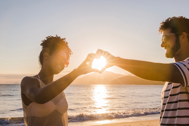 Photo gratuite couple formant coeur avec les mains au coucher du soleil