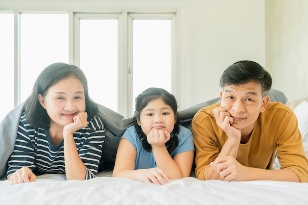 Couple de grands-parents seniors asiatiques portant avec des petits-enfants preety enfant de sexe féminin sur le lit dans la chambre à coucherfamille heureuse jouer ensemble dans le lit