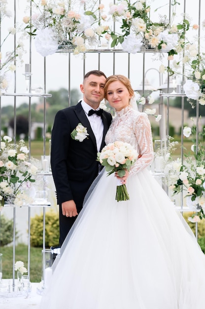 Couple heureux le jour du mariage posant sur l'autel fleuri à l'extérieur