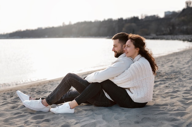 Photo gratuite couple heureux plein coup assis sur la plage