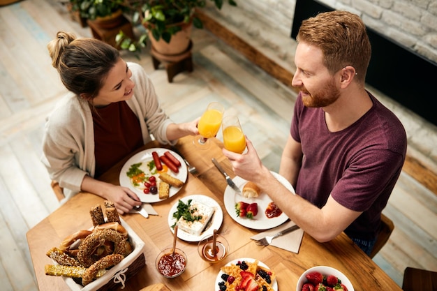 Couple heureux portant un toast avec du jus d'orange pendant le petit déjeuner à la maison