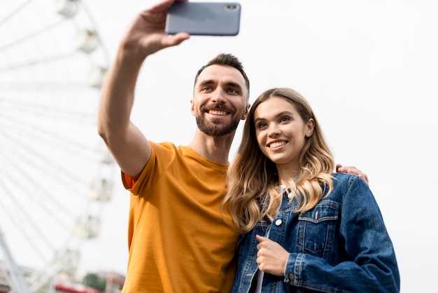 Photo gratuite couple heureux de prendre une photo de soi devant la grande roue