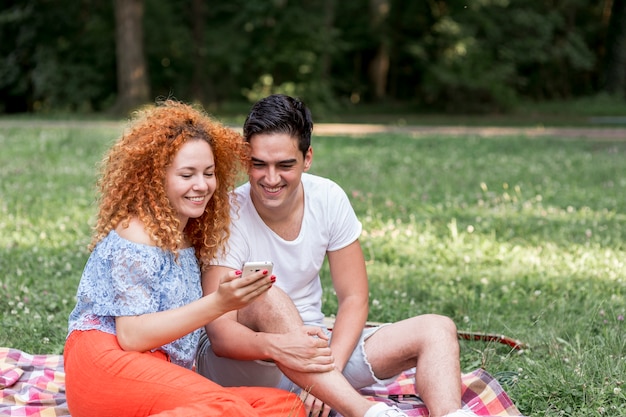 Couple heureux se détendre et vérifier le téléphone dans le parc