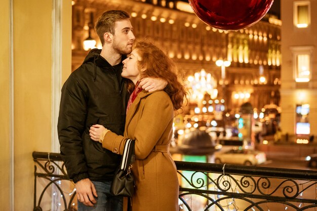 Un couple heureux se tient dans une étreinte dans la rue le soir dans les lumières de fête