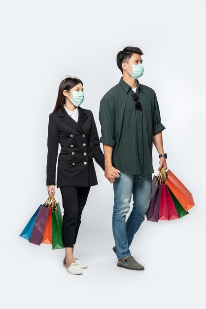 Un couple d'hommes et de femmes portant des masques et transportant beaucoup de sacs en papier pour faire du shopping