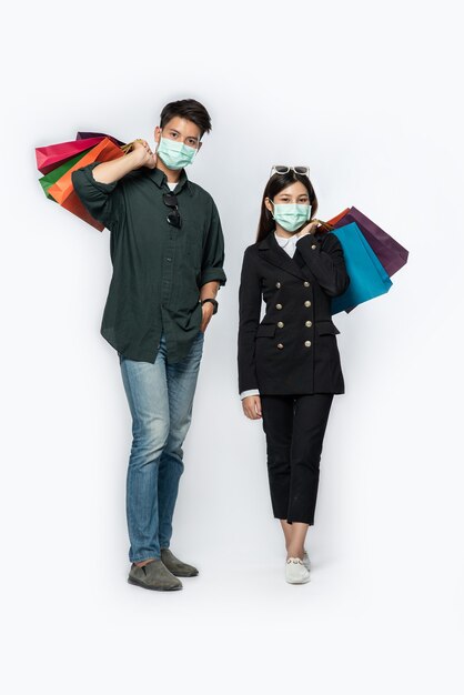 Un couple d'hommes et de femmes portant des masques et transportant beaucoup de sacs en papier pour faire du shopping