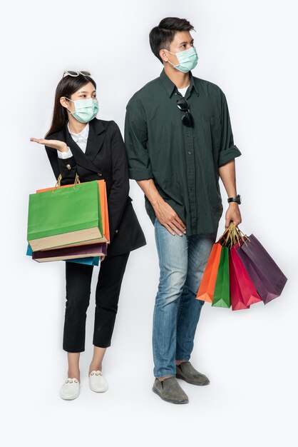 Un couple d'hommes et de femmes portant des masques et transportant beaucoup de sacs en papier pour faire du shopping