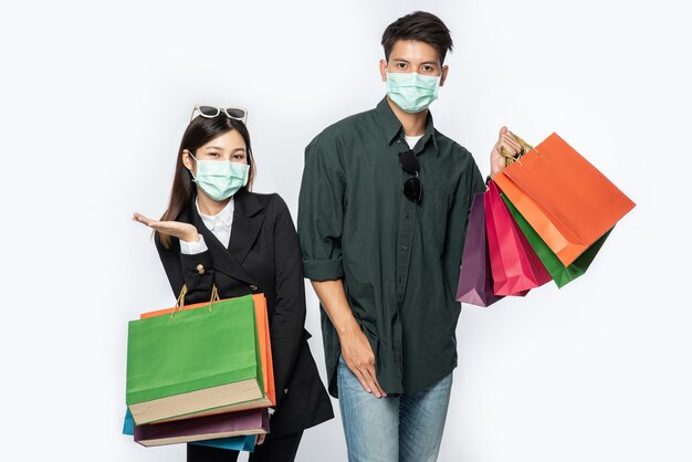 Un couple d'hommes et de femmes portant des masques et transportant beaucoup de sacs en papier pour faire du shopping