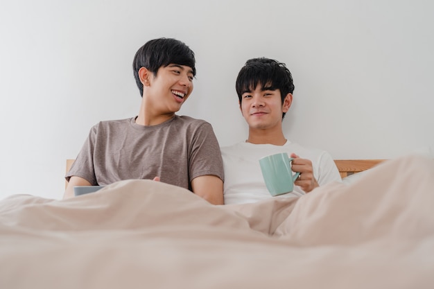 Couple d'hommes homosexuels asiatiques parlant d'avoir un bon moment à la maison moderne. Jeune amant asiatique mâle heureux se détendre reste boire un café après le réveil en position couchée sur un lit dans la chambre à la maison à la maison le matin.