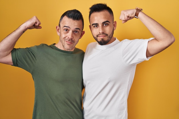 Photo gratuite couple homosexuel debout sur fond jaune personne forte montrant le muscle du bras confiant et fier du pouvoir