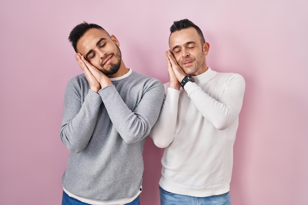 Couple homosexuel debout sur fond rose dormant fatigué rêvant et posant avec les mains ensemble tout en souriant les yeux fermés