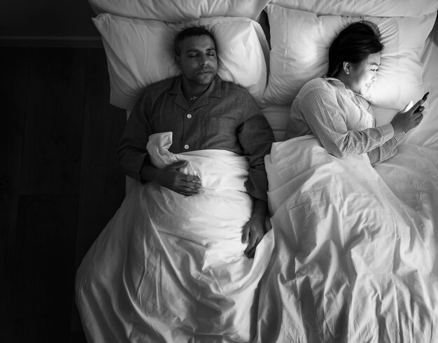 Couple interracial sur la femme du lit en utilisant son téléphone
