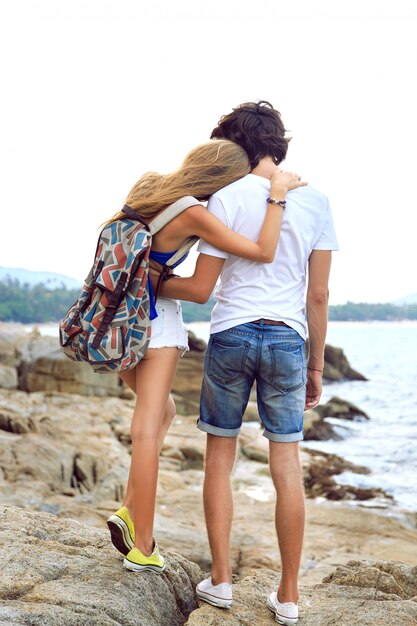 Couple de jeunes hipster amoureux voyagent ensemble en été, posant sur une magnifique plage de pierre, portant des tenues décontractées élégantes, des câlins et s'amusant.
