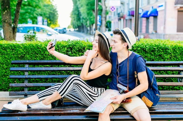 Couple de jeunes touristes sur un banc prenant un selfie