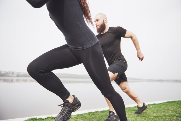 Couple jogging et courir à l'extérieur dans le parc près de l'eau. Jeune homme barbu et femme exerçant ensemble le matin