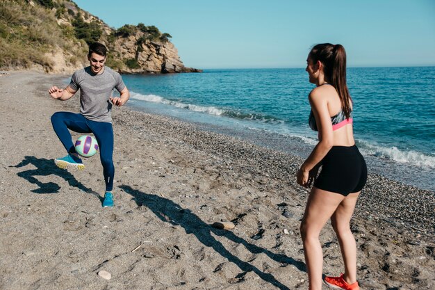 Couple jouant au football à la plage