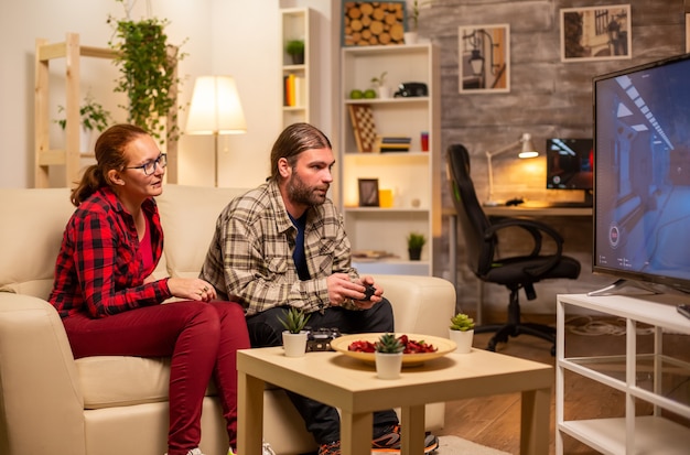 Couple jouant à des jeux vidéo sur un téléviseur grand écran dans le salon tard dans la nuit.