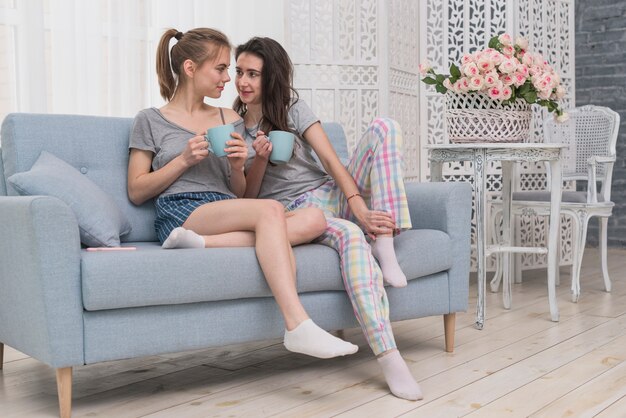 Couple lesbien, tenue, tasse café, séance, sur, sofa, regarder, autre