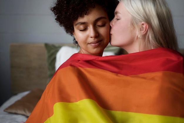 Photo gratuite un couple de lesbiennes s'embrasse avec un drapeau lgbt