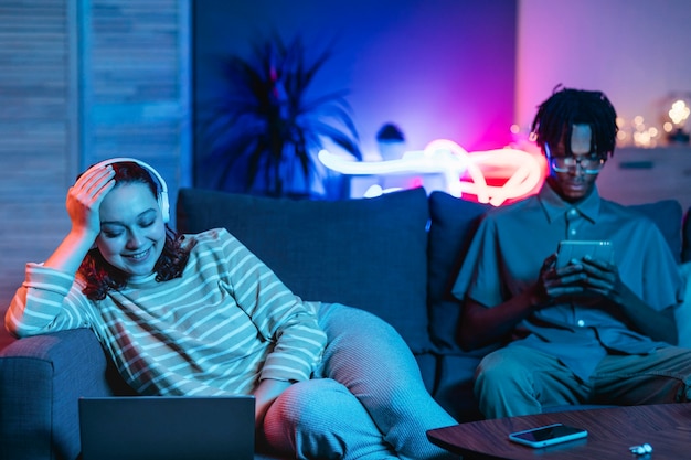 Couple à la maison ensemble sur le canapé à l'aide d'appareils modernes