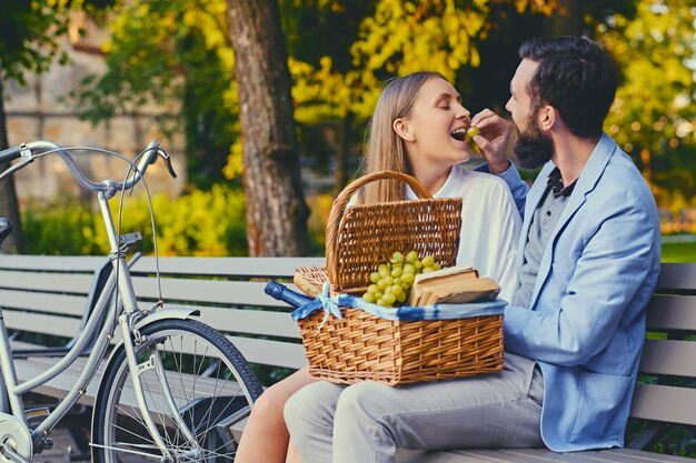 Un couple mange du raisin sur un banc dans un parc.