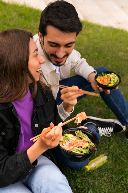 Photo gratuite couple mangeant un bol de saumon sur l'herbe à l'extérieur