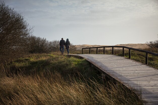 Couple marchant sur un pont en bois entouré d'un champ et de collines sous la lumière du soleil