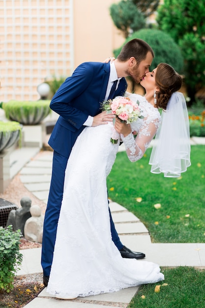 Photo gratuite couple de mariage amoureux s'embrassant et souriant. jeune mariée assez élégante et son beau marié posant dans le parc verdoyant.