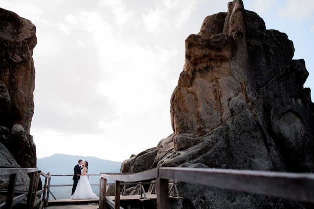 Couple de mariage est debout sur le pont en bois entre deux hautes falaises et baisers, aventure de mariage