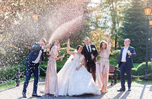 Couple de mariage et meilleurs amis boivent du champagne et célèbrent dans le parc le jour du mariage