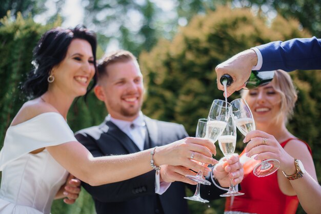 Couple de mariage souri avec les meilleurs amis boivent du champagne à l'extérieur et souriant